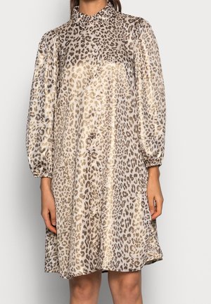 Langærmet skjortekjole med skinnende beige og brun leopardprint, løs pasform og opsamlede ærmekanter, båret af en stående person.