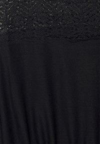 Tissu noir avec un détail en dentelle horizontale présentant des motifs floraux et géométriques sur le bord supérieur.