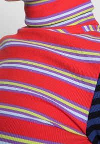 Rød rullekravesweater med fine horisontale striber i lilla, lyseblå og grøn. Ribbet tekstur med tætsiddende design.
