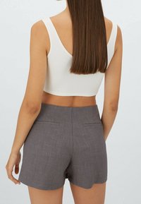 Grijze op maat gemaakte shorts met twee achterzakken, gecombineerd met een witte ribbelige crop top. Stof is glad; shorts hebben een schone, gestructureerde uitstraling.