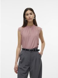 Top rosa senza maniche con dettagli in pizzo sulle spalle, caratterizzato da un collo alto e una scollatura a chiave. Abbinato a pantaloni grigi a vita alta e una cintura nera.