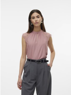 Haut sans manches rose avec des détails en dentelle aux épaules, comportant un col haut et un décolleté en trou de serrure. Assorti à un pantalon gris taille haute et une ceinture noire.