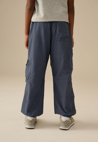 Pantaloni cargo blu navy con una vestibilità ampia, numerose tasche e una sottile lucentezza. Abbinati a sneakers grigio chiaro e una maglietta grigia casual.