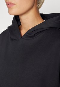 Felpa nera con una texture morbida e un scollo ampio. Presenta un cappuccio ripiegato discreto e una vestibilità morbida, ideale per un look informale.