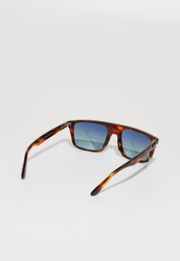 Lunettes de soleil à monture écaille avec verres rectangulaires dégradés bleus, présentées de dos sur un fond blanc.