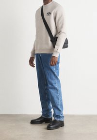 Gray sweatshirt with embroidered logo, blue loose jeans, and black ankle boots, complemented by a black crossbody bag.