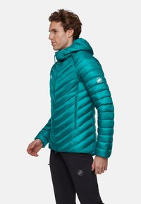 Teal pufferjakke med hætte; har chevronmønster, lynlåslommer og logo på ærmet; lavet af letvægtsmateriale.