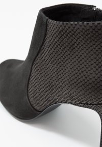 Stivaletto nero con una combinazione di suede liscio e materiale testurizzato con motivo serpente, dotato di un tacco elegante e dettaglio della cerniera laterale.