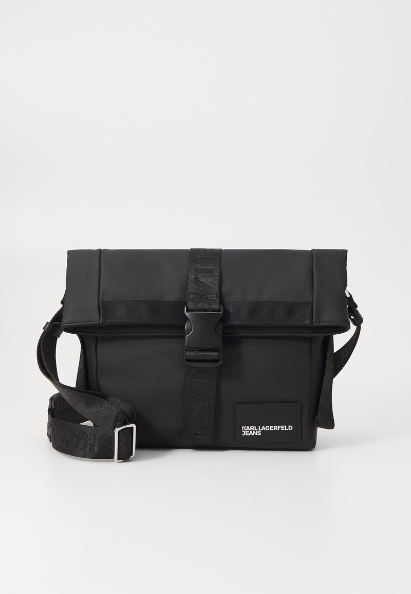 Borsa a tracolla nera con chiusura a pattina, realizzata in materiale liscio. Caratterizzata da una tracolla regolabile, hardware a fibbia e logo sul fronte.