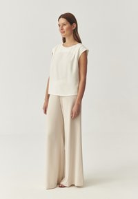 Pantalones anchos de color beige combinados con una blusa de manga corta en tono crema. El tejido parece suave, con un diseño minimalista y un ajuste relajado.