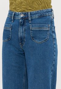 Jeans de ganga azul com um design clássico de cinco bolsos, featuring um fecho de botão, ligeira descoloração e um corte reto.