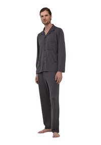 Pigiama grigio a maniche lunghe realizzato in tessuto morbido. Camicia con bottoni e taschino sul petto. Pantaloni larghi con cintura elastica.