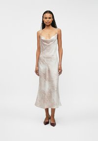 Φόρεμα slip με λαιμό cowl σε ανοιχτό μπεζ χρώμα με διακριτό μοτίβο ζωντανών. Διαθέτει λεπτές τιράντες και ρέον ύφασμα που πέφτει κομψά.