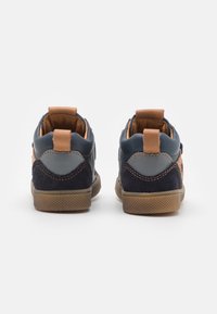 Des chaussures montantes bleu marine et beige, alliant cuir et daim, avec des accents cousus et une semelle en caoutchouc texturée.