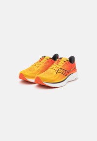 Baskets de sport jaunes et oranges avec une tige en maille, des accents texturés et une semelle blanche rembourrée. Détails noirs au talon et à la languette.
