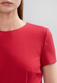 Haut rouge à manches courtes fabriqué en tissu texturé, avec un col rond et des détails de couture subtils, mettant en avant un design lisse et épuré.