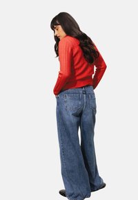 Pull en maille côtelée rouge à longues manches, associé à un jean large à taille haute bleu clair, décontracté, avec poches arrière et un design piqué.