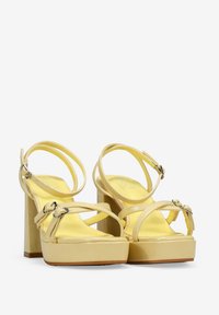 Sandalias de plataforma de charol amarillo con tiras delgadas y hebillas en el tobillo, con un tacón grueso y plantilla acolchada.