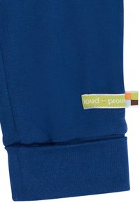 Blaue Baumwoll-Sweatpants mit einem gerippten Bündchen, das an der linken Seite ein mehrfarbiges "loud + proud"-Label hat. Weicher Stoff, lässiger Schnitt.