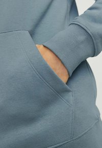 Blauwe katoenen hoodie met een voorknoop en ribgebreide manchetten. De stof heeft een soepele textuur met zichtbare stikseldetails.