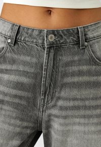 Grå denimjeans med en lätt sliten struktur, med metalldragknapp och standard bältesöglor.