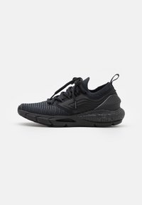 Zapatilla deportiva negra con parte superior de punto, suela acolchada, parte frontal con cordones y lazo en el talón, mostrada en perfil lateral sobre un fondo blanco.