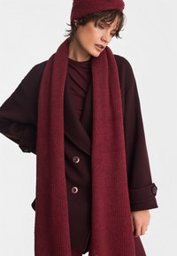 Burgundzka szalik o prążkowanej fakturze, zestawiony z głęboko czerwonym, oversize'owym płaszczem z dużymi guzikami i warstwową górą.