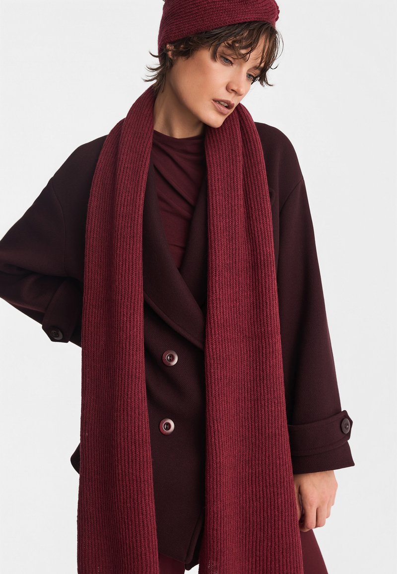 Burgundzka szalik o prążkowanej fakturze, zestawiony z głęboko czerwonym, oversize'owym płaszczem z dużymi guzikami i warstwową górą.