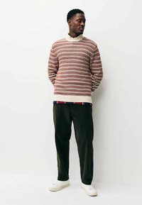Knitted red and cream sweater with a ribbed collar, layered over a striped shirt, paired with dark green corduroy pants and white sneakers.