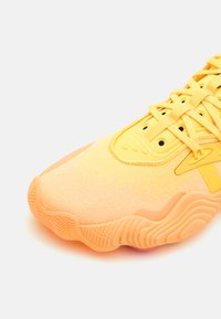 Baskets de sport jaunes vives présentant un dessus en tissu texturé, une semelle en caoutchouc avec des motifs ondulés, et un design à lacets avec des œillets circulaires.
