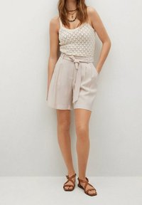 Shorts beige a vita alta con cintura legata, abbinati a una canotta bianca in maglia. Sandali beige con cinturini completano l'outfit.