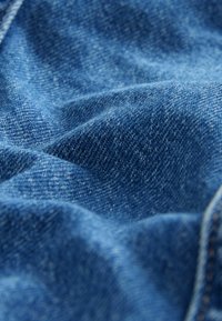 Denimtyg i djupblått med en strukturerad väv, som visar subtila färg- och ljusvariationer. Slät yta med naturliga veck.