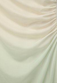 Hellgrüner Stoff mit sanften Falten und einer glatten Textur, dezentem Glanz und einem zarten Fall. Nahtdetails verleihen Tiefe.