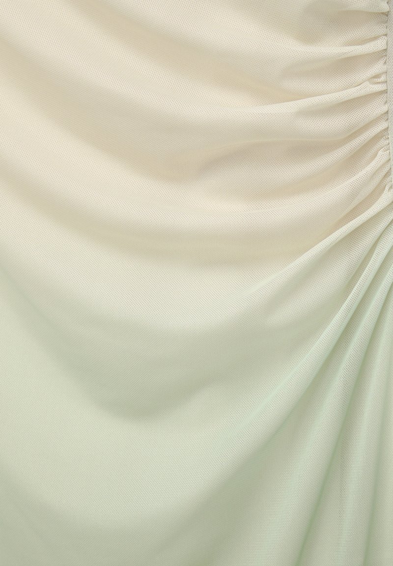 Tissu vert clair présentant de doux plis et une texture lisse, avec un éclat subtil et une drapé délicat. Les coutures ajoutent de la profondeur.