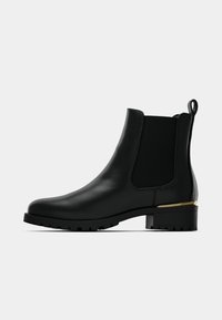 Černá kožená kotníková bota s elastickými bočními panely, kulatou špičkou, texturovanou gumovou podrážkou a zlatým detailem na patě.