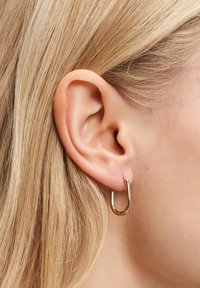 Nahaufnahme eines Ohres einer blonden Person, die einen kleinen, glänzenden goldenen Hänger trägt.