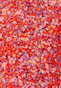 Tissu éclatant avec un motif floral dense de rouge, rose et violet, agrémenté de petites perles argentées verticales dispersées uniformément.