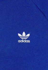 Modrá bavlněná mikina s bílým vyšívaným logem Adidas, které zobrazuje tři pruhy a list s třemi cípy na hrudi.