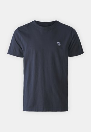 T-shirt en coton bleu marine avec un col rond, des manches courtes et un petit design brodé sur la poitrine gauche. Texture lisse, coupe décontractée.