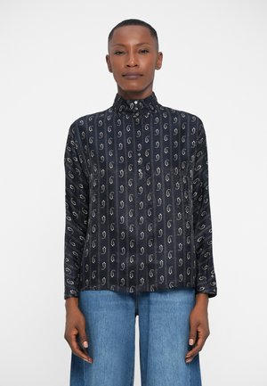 Chemise à manches longues bleu marine avec un col haut, ornée de motifs verticaux blancs et de boutons sur le devant. Portée sur un jean large bleu clair.