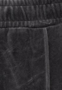 Svart plyschtyg med en mjuk textur, med en bred elastisk midjeband och en vertikal sömdetalj. Mjuk och bekväm design.