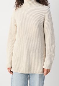Crème-kleurige, chunky gebreide coltrui met geribbelde textuur en verlaagde schouders. Bevat lange mouwen en heeft een ontspannen pasvorm.