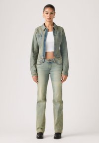 Σετ τζιν μπουφάν και τζιν παντελόνι σε ανοιχτό μπλε-πράσινο χρώμα, με cropped σχεδιασμό, μπροστινές τσέπες και κλείσιμο με φερμουάρ. Μαύρες μπότες ολοκληρώνουν την εμφάνιση.