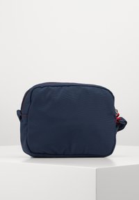 Marlová modrá textilní taštička obdélníkového tvaru, sezipovým uzávěrem, červenými švy a bočním madlem pro snadné přenášení.