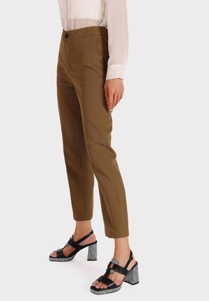 Pantaloni marroni su misura con una vestibilità slim, abbinati a sandali neri con tacco a blocco decorato e cinturini alla caviglia.