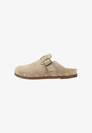 Zapato tipo zueco beige de ante sin cordones, con correa ajustable con hebilla y tachuelas redondas doradas a lo largo del borde, suela plana marrón.