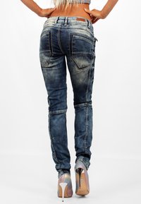 Jeans skinny in denim blu sbiadito con cuciture a contrasto e numerosi taschini, abbinati a scarpe col tacco iridescenti.