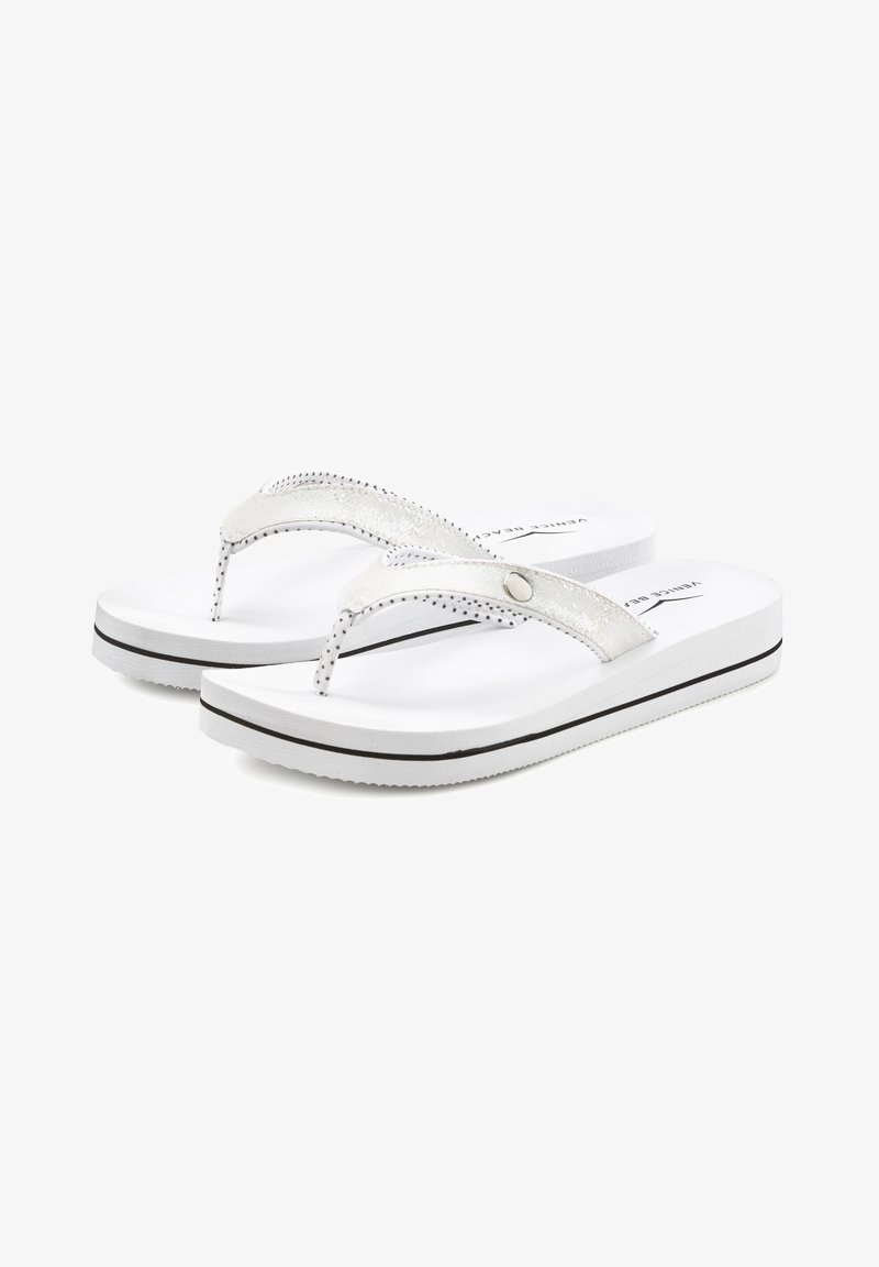 Des tongs blanches avec une sangle métallique argentée texturée, soulignée de coutures noires, et une semelle rembourrée présentant une ligne noire horizontale.