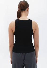 Top de tirantes negro con un diseño ajustado, tirantes anchos y escote redondo, combinado con pantalones gris sueltos.