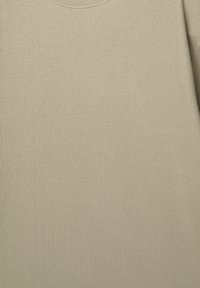 Beige tekstureret stof med et ribbet mønster, der har en rund halsudskæring og lange ærmer. Materialet fremstår blødt og strækbart.